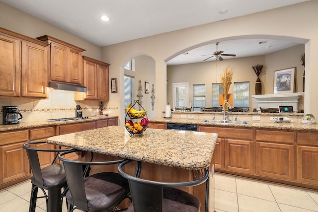 kitchen with ceiling fan, sink, light stone counters, kitchen peninsula, and a kitchen bar