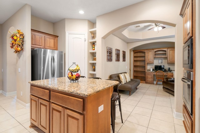 kitchen featuring ceiling fan, stainless steel appliances, a kitchen island, light stone counters, and light tile patterned flooring