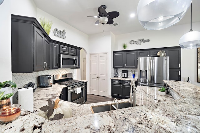 kitchen featuring decorative backsplash, light stone countertops, stainless steel appliances, and hanging light fixtures