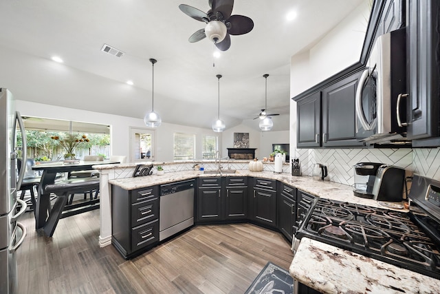 kitchen featuring kitchen peninsula, appliances with stainless steel finishes, pendant lighting, and lofted ceiling