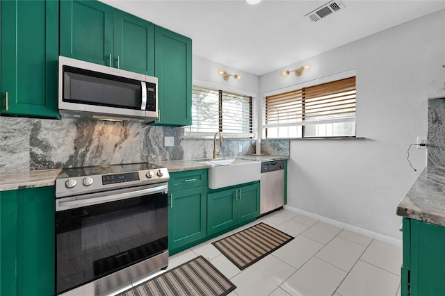 kitchen featuring sink, light stone counters, appliances with stainless steel finishes, green cabinets, and decorative backsplash