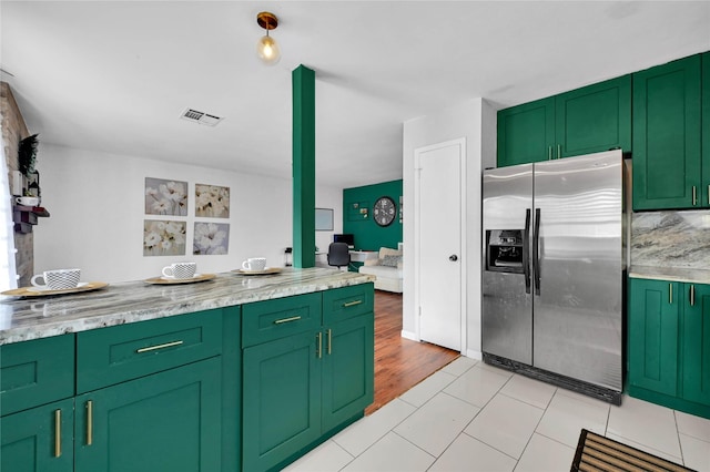 kitchen featuring green cabinets, light stone countertops, and stainless steel fridge with ice dispenser