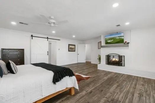 bedroom featuring a multi sided fireplace, dark hardwood / wood-style flooring, a barn door, and ceiling fan