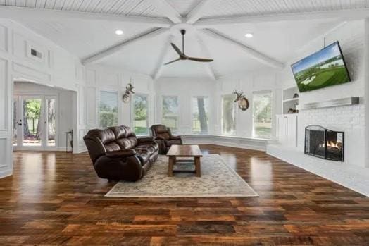 living room with built in shelves, beamed ceiling, dark wood-type flooring, and a brick fireplace