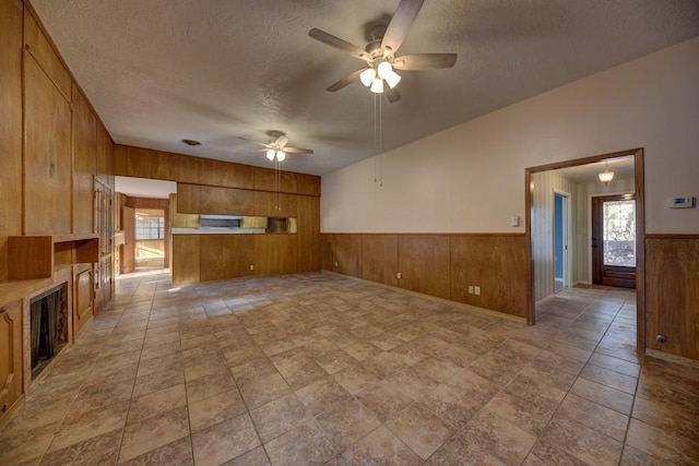 unfurnished living room featuring a textured ceiling, ceiling fan, and wooden walls