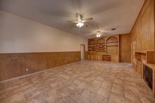 unfurnished living room featuring built in shelves, built in desk, a textured ceiling, and wood walls