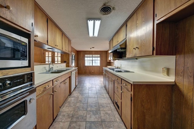 kitchen featuring a textured ceiling, wooden walls, sink, and appliances with stainless steel finishes