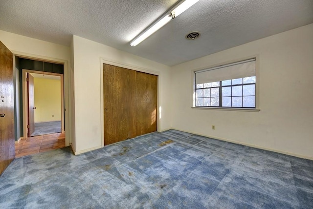 unfurnished bedroom with a closet, a textured ceiling, and dark colored carpet