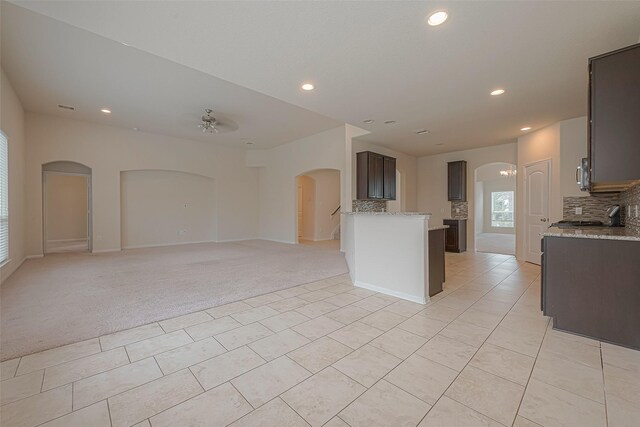 kitchen featuring dark brown cabinetry, ceiling fan, light stone countertops, backsplash, and light colored carpet