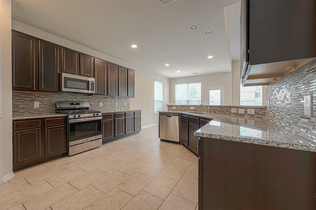 kitchen featuring dark brown cabinets, light stone countertops, backsplash, and appliances with stainless steel finishes