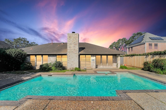 pool at dusk with a patio area and an in ground hot tub