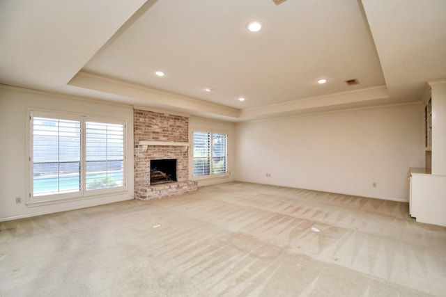 unfurnished living room featuring a raised ceiling, light colored carpet, crown molding, and a brick fireplace