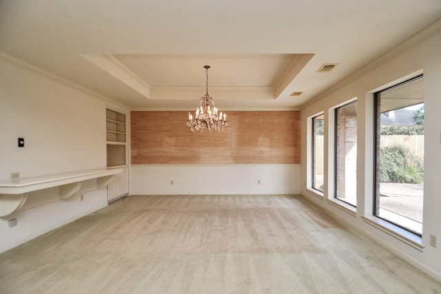 empty room featuring built in shelves, an inviting chandelier, crown molding, a tray ceiling, and carpet floors