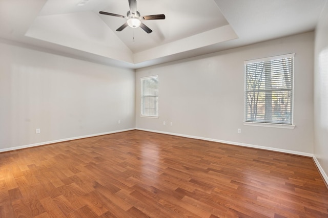 empty room with hardwood / wood-style flooring, ceiling fan, and a tray ceiling