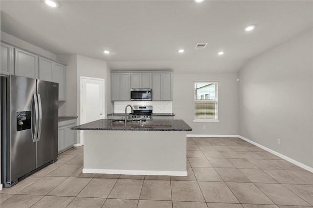 kitchen with light tile patterned flooring, stainless steel appliances, a kitchen island with sink, and dark stone countertops