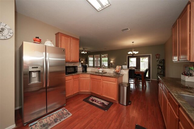 kitchen with pendant lighting, ceiling fan with notable chandelier, stainless steel refrigerator with ice dispenser, dark hardwood / wood-style floors, and kitchen peninsula