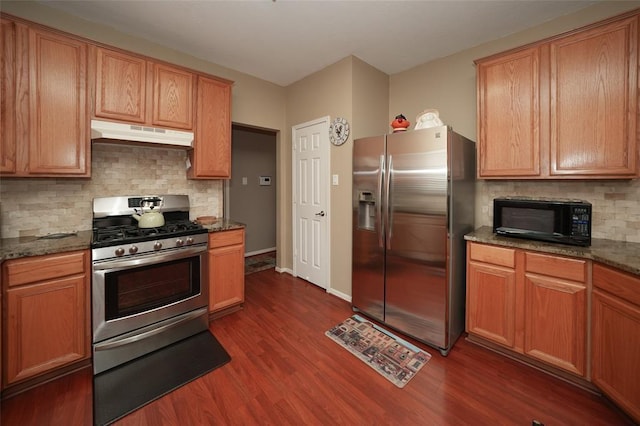 kitchen featuring dark stone countertops, decorative backsplash, dark wood-type flooring, and appliances with stainless steel finishes