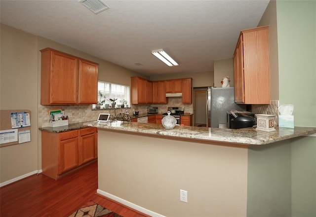 kitchen featuring kitchen peninsula, appliances with stainless steel finishes, decorative backsplash, light stone counters, and dark hardwood / wood-style floors