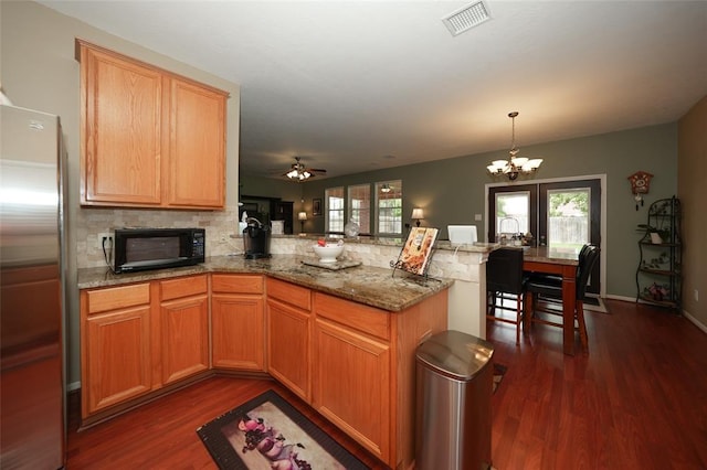 kitchen featuring ceiling fan with notable chandelier, stainless steel fridge, dark hardwood / wood-style flooring, and kitchen peninsula