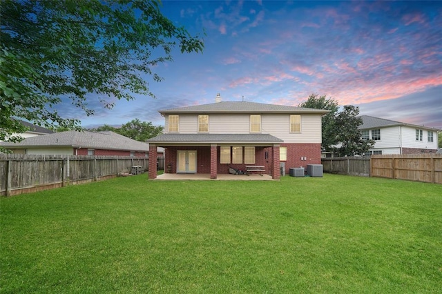 back house at dusk with a lawn, a patio area, and central AC unit