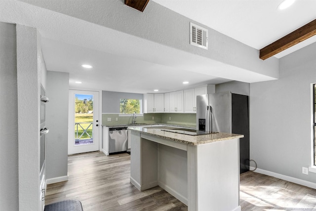 kitchen featuring appliances with stainless steel finishes, white cabinets, light stone counters, beamed ceiling, and a center island