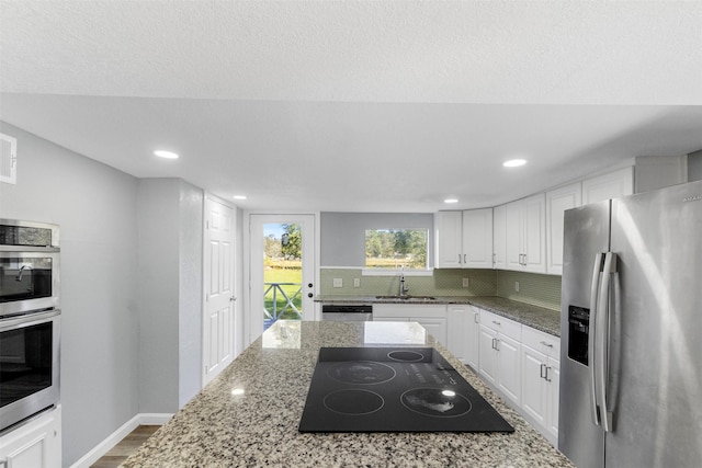 kitchen featuring tasteful backsplash, white cabinetry, stainless steel appliances, and light stone counters