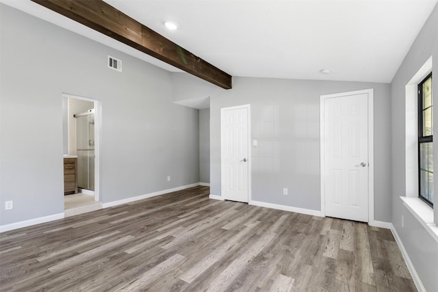 unfurnished bedroom with lofted ceiling with beams, ensuite bathroom, multiple windows, and light hardwood / wood-style floors