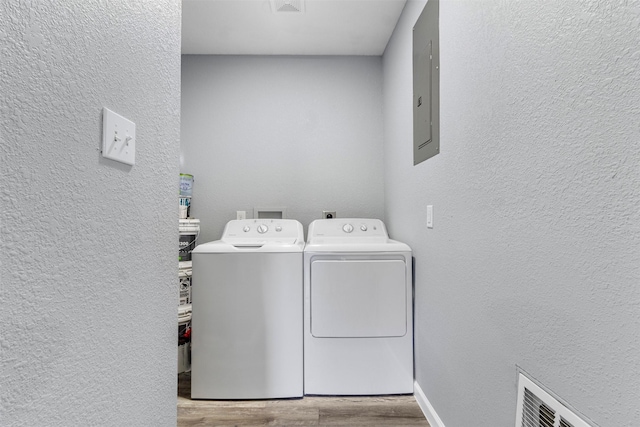 washroom featuring light wood-type flooring, electric panel, and washing machine and clothes dryer