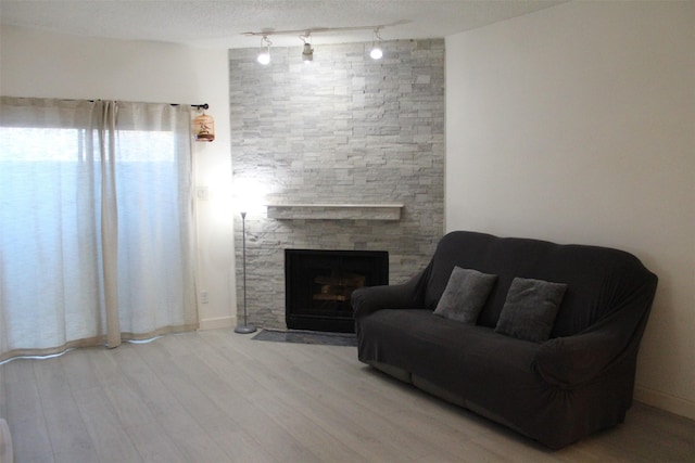 living room with a fireplace, a textured ceiling, track lighting, and light hardwood / wood-style flooring