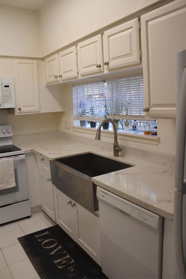 kitchen featuring white cabinetry, sink, light stone countertops, white appliances, and light tile patterned flooring