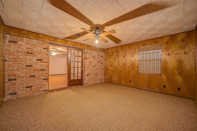 carpeted spare room with ceiling fan, wood walls, and brick wall