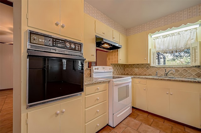 kitchen with cream cabinets, sink, electric range, black oven, and light tile patterned flooring