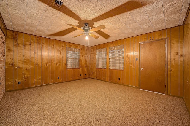 unfurnished room featuring ceiling fan, wooden walls, and carpet floors