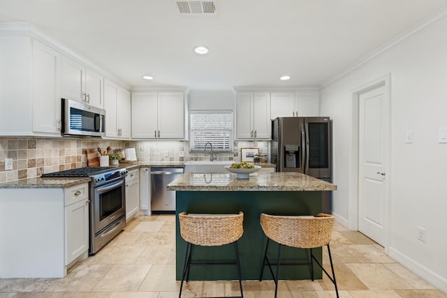 kitchen with a center island, stainless steel appliances, white cabinetry, and light stone counters