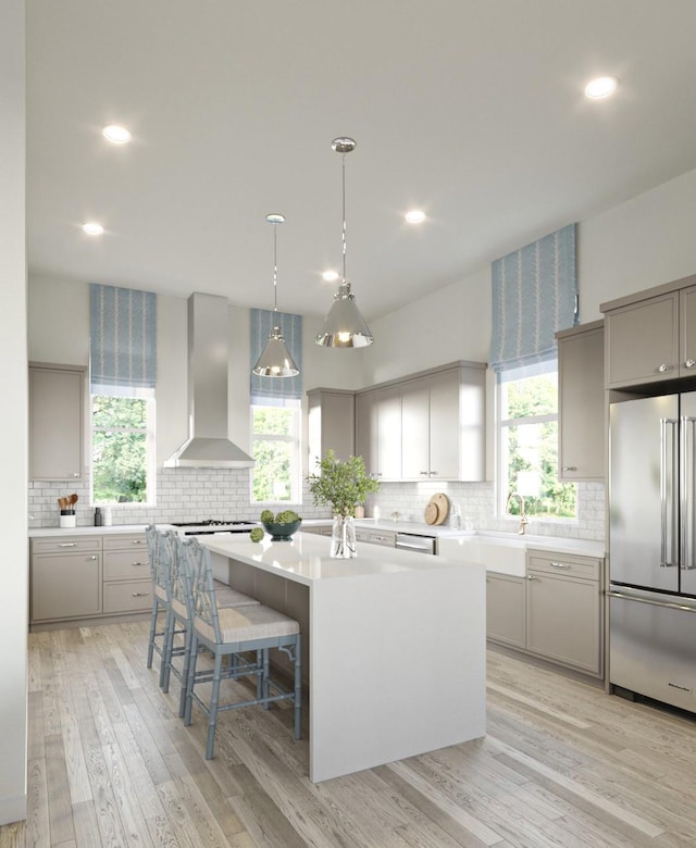 kitchen featuring high end refrigerator, gray cabinetry, a breakfast bar, wall chimney range hood, and a center island with sink