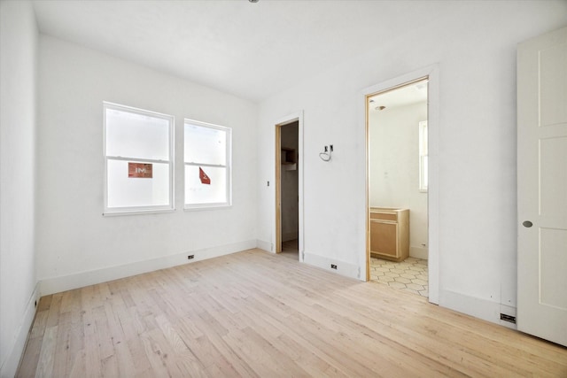 unfurnished bedroom featuring a walk in closet, ensuite bathroom, and light hardwood / wood-style flooring