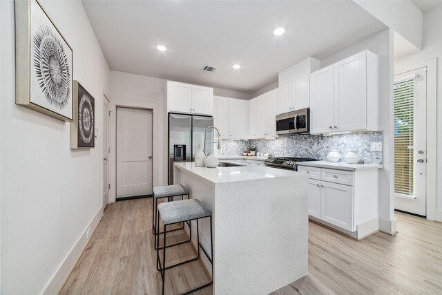 kitchen featuring a breakfast bar, stainless steel appliances, sink, white cabinets, and an island with sink