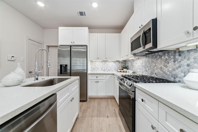 kitchen with decorative backsplash, appliances with stainless steel finishes, sink, light hardwood / wood-style floors, and white cabinetry