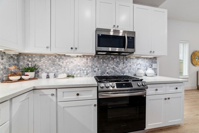 kitchen with backsplash, stainless steel appliances, white cabinetry, and light hardwood / wood-style floors