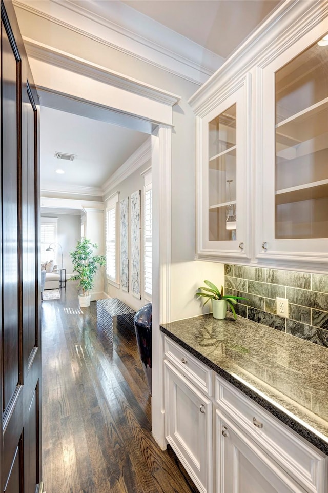 bar featuring crown molding, white cabinetry, tasteful backsplash, dark hardwood / wood-style flooring, and dark stone counters