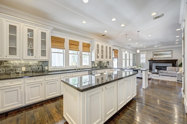 kitchen featuring white cabinetry, decorative light fixtures, a tile fireplace, and dark stone countertops