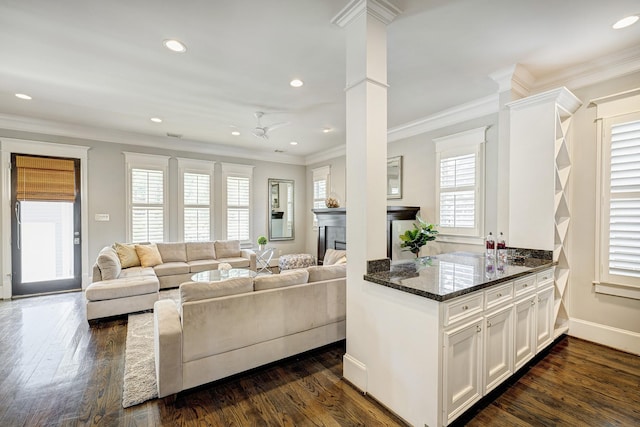 living room featuring dark wood-type flooring, ceiling fan, crown molding, and decorative columns