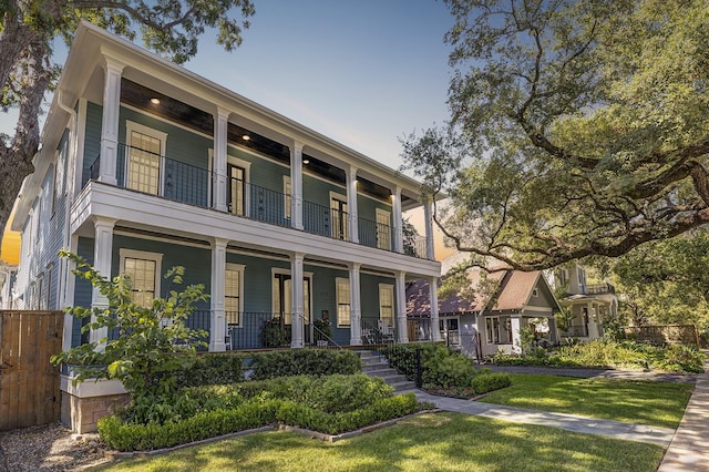 view of front of home featuring a front yard, a balcony, and covered porch