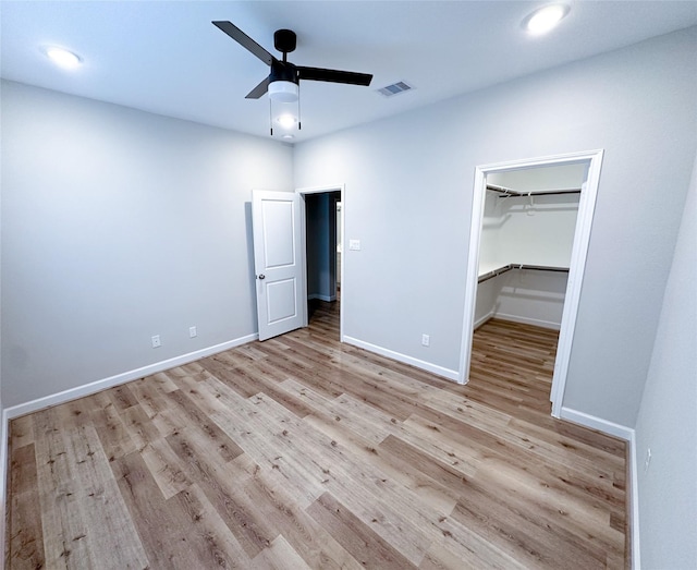 unfurnished bedroom with a walk in closet, a closet, light hardwood / wood-style flooring, and ceiling fan