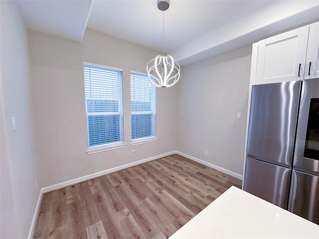 kitchen featuring pendant lighting, stainless steel fridge, light wood-type flooring, a notable chandelier, and white cabinetry