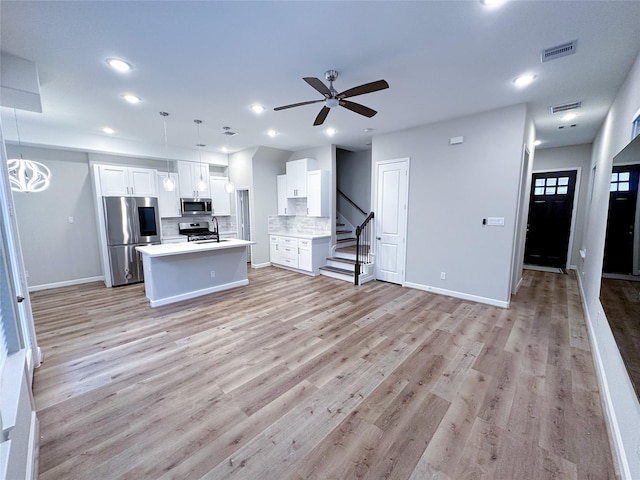 kitchen featuring white cabinetry, backsplash, decorative light fixtures, a kitchen island with sink, and appliances with stainless steel finishes