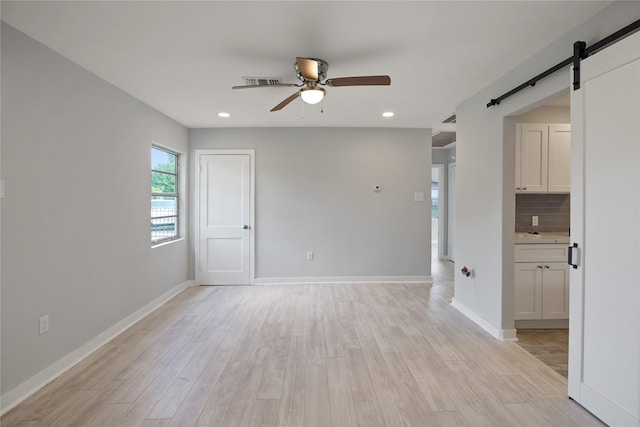 spare room featuring a barn door, light hardwood / wood-style flooring, and ceiling fan