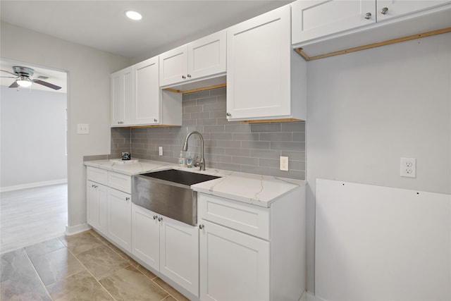 kitchen featuring white cabinets, ceiling fan, light stone countertops, and sink