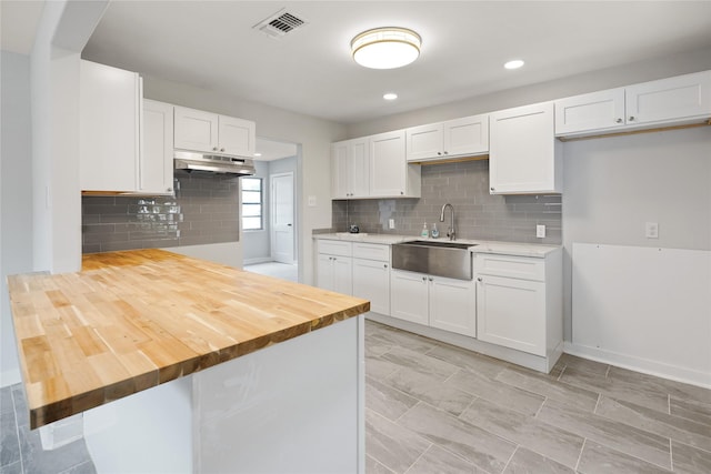 kitchen with decorative backsplash, white cabinetry, sink, and wood counters