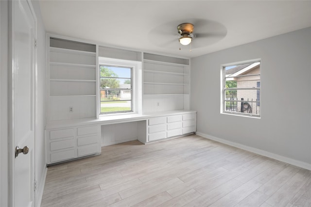 unfurnished office featuring built in shelves, built in desk, light hardwood / wood-style floors, and ceiling fan